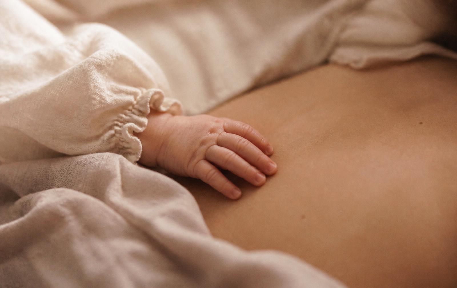 Mano del bebé recién nacido apoyada sobre la piel de su madre